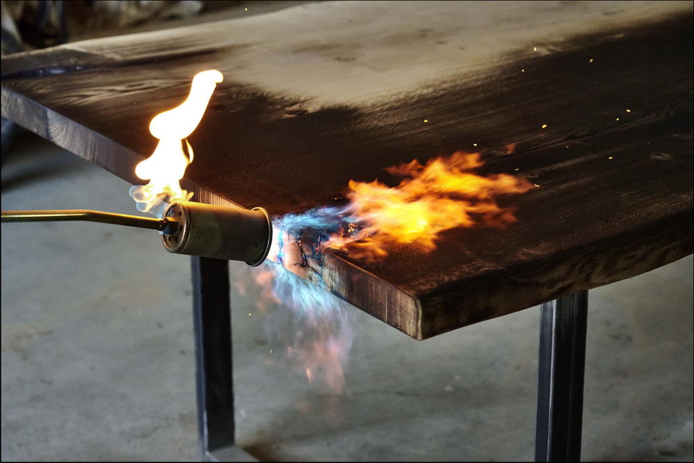 Chalumeau en train de brûler une table en bois brut pour faire une belle table noircie avec la méthode du Shou Sugi Ban